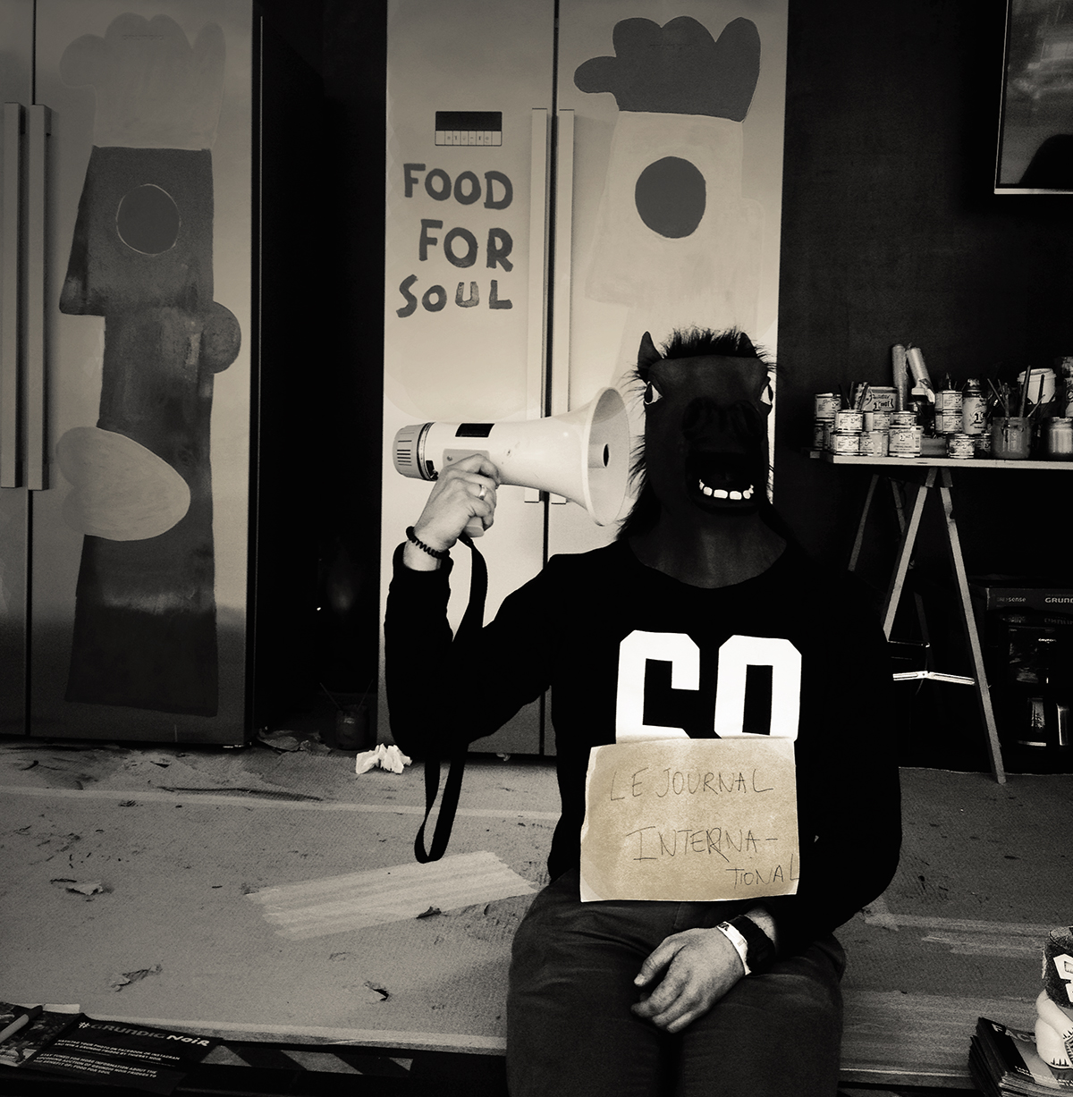 Collègue de Thierry Noir plaisantant avec un masque et posant devant les frigos en train d’être peints dans le cadre du projet Grunding. Il tient dans ses mains une affichette fabriquée pour le Journal International - Crédit Chloé Marchal